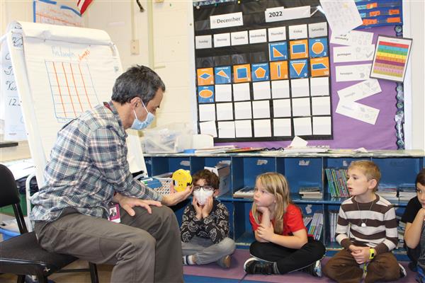  first grade students look on with interest at the BeeBot programmable robot held by their teacher 