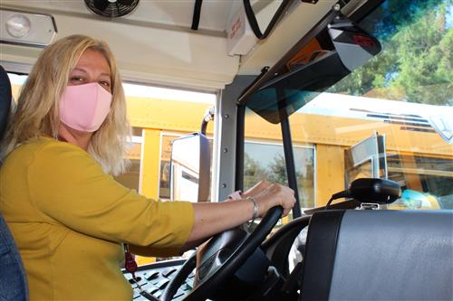 woman in yellow shirt wearing a mask driving bus 