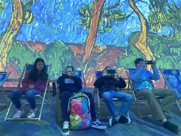  students sitting in lawnchairs with colorful background 
